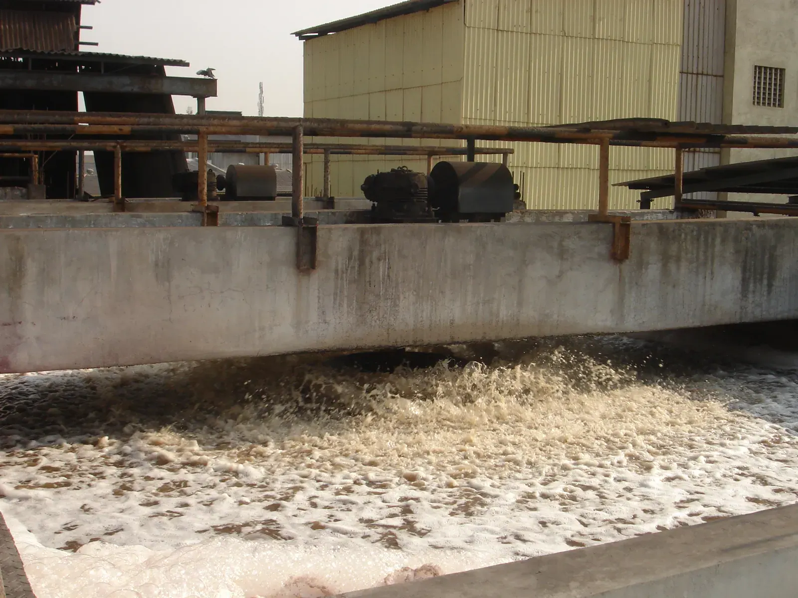 A surface aerator churning the water of an aeration basin, below a service walkway.