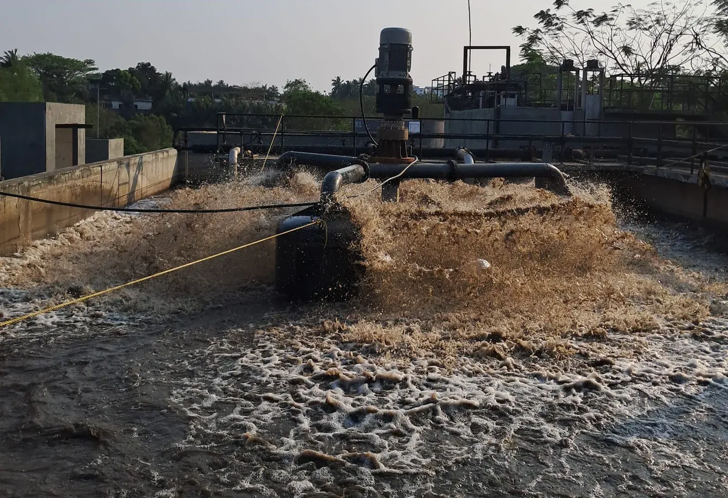 An aeration basin in operation: a surface aerator throwing brown spray, the far walls of the basin behind it.