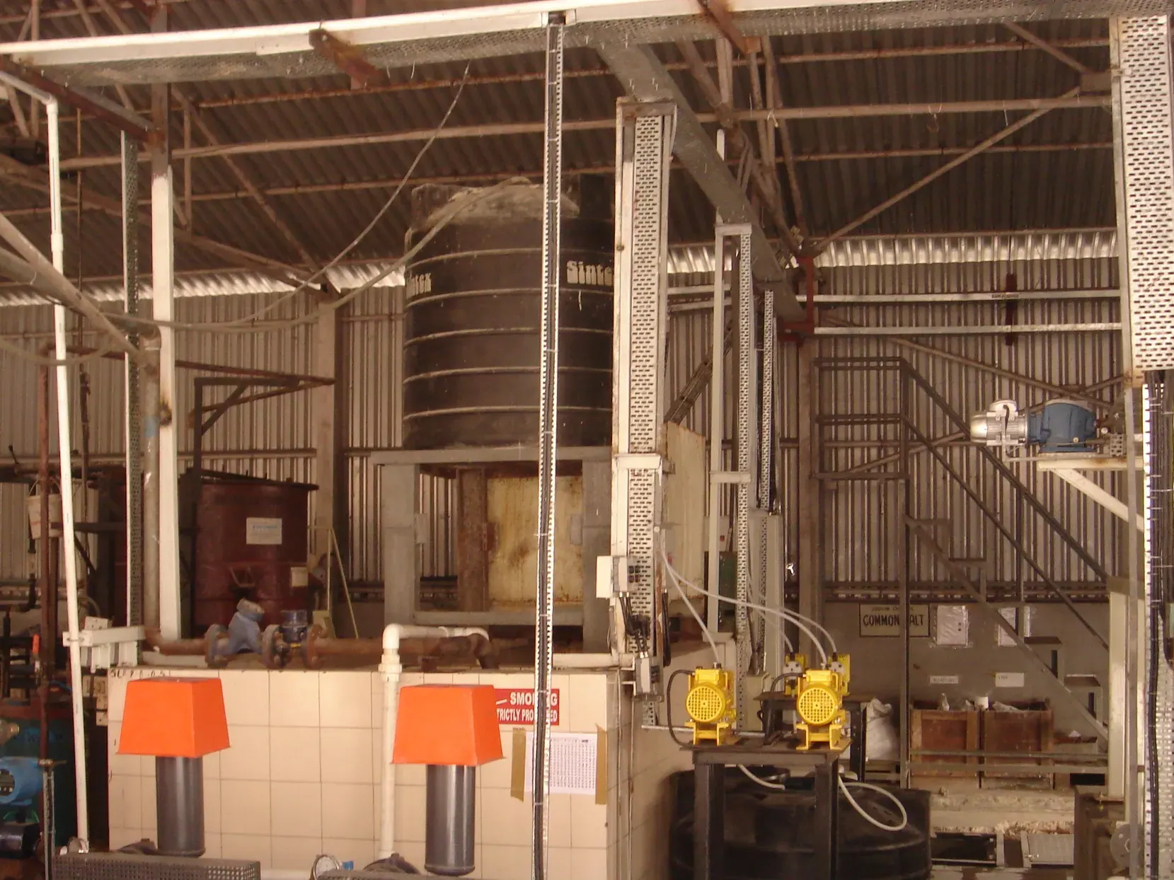 Inside a treatment plant building: air blowers, dosing pumps and chemical tanks under a sheet roof.